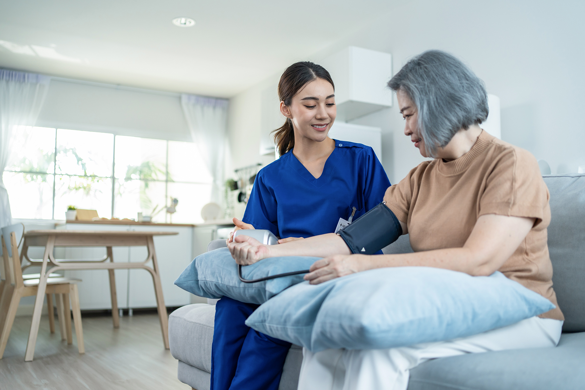 Asian caregiver doctor examine older patient use blood pressure gauge. Young woman therapist nurse at nursing home taking care of senior elderly woman sit on sofa. Medical insurance service concept