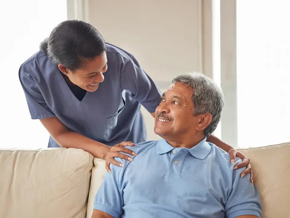Nurse providing care and support to an elderly man on a sofa